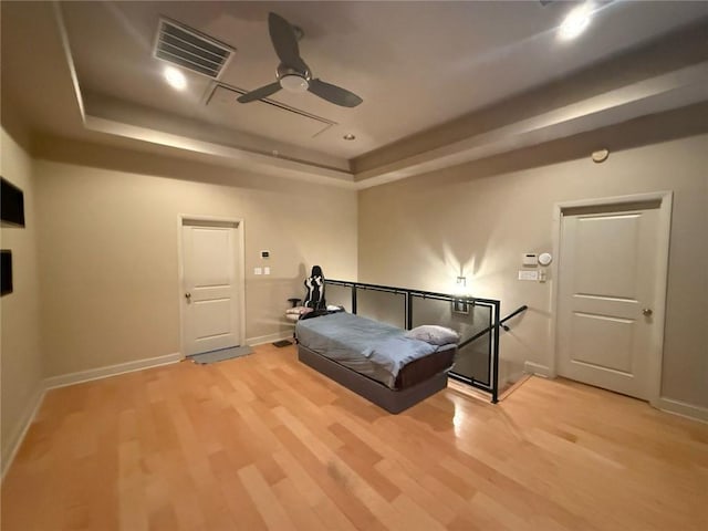 bedroom with ceiling fan, light wood-type flooring, and a tray ceiling