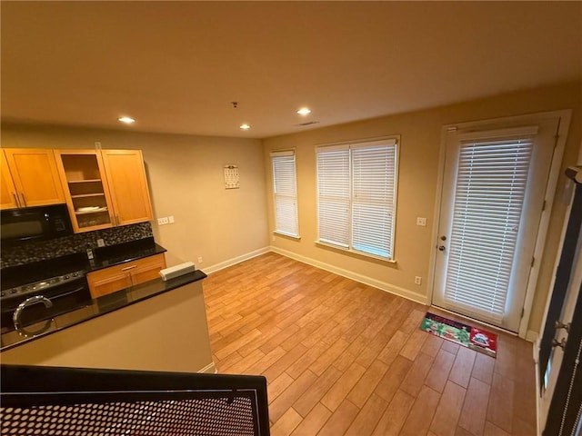 kitchen featuring light wood-type flooring, oven, light brown cabinetry, and decorative backsplash