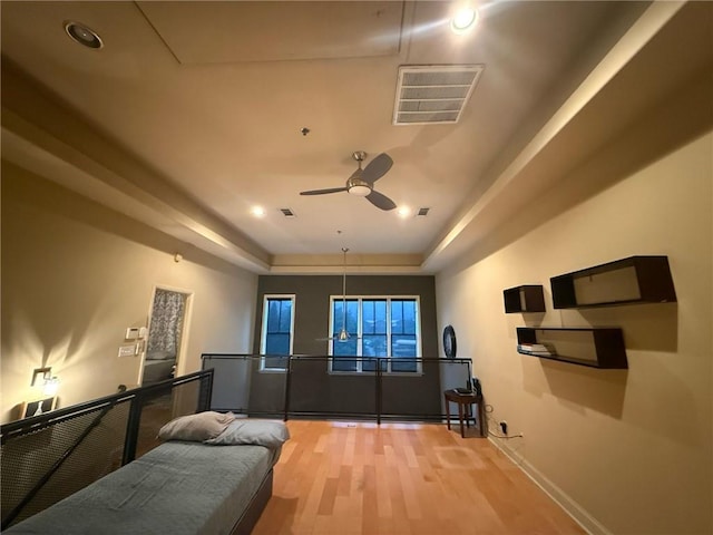 cinema room featuring hardwood / wood-style flooring, ceiling fan, and a tray ceiling