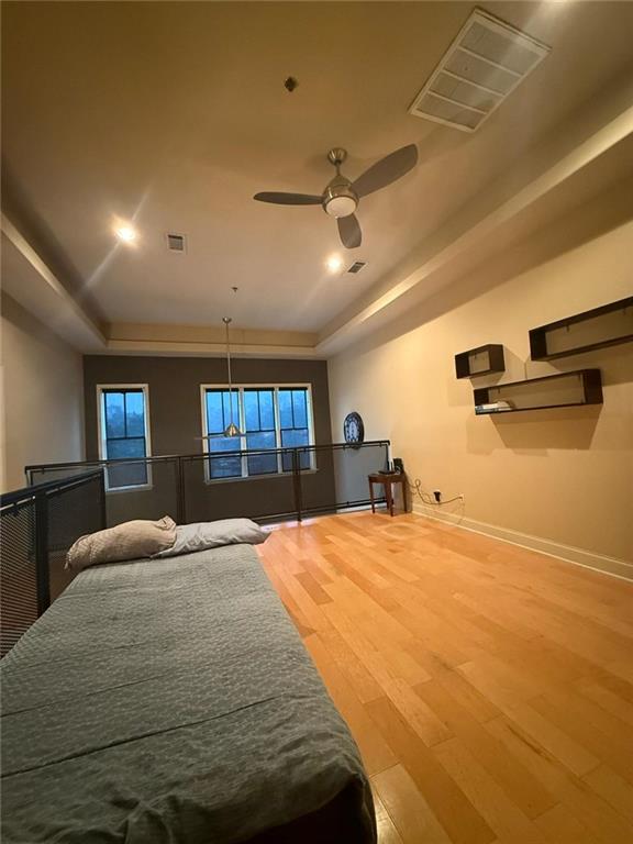 bedroom with ceiling fan, a tray ceiling, and hardwood / wood-style floors