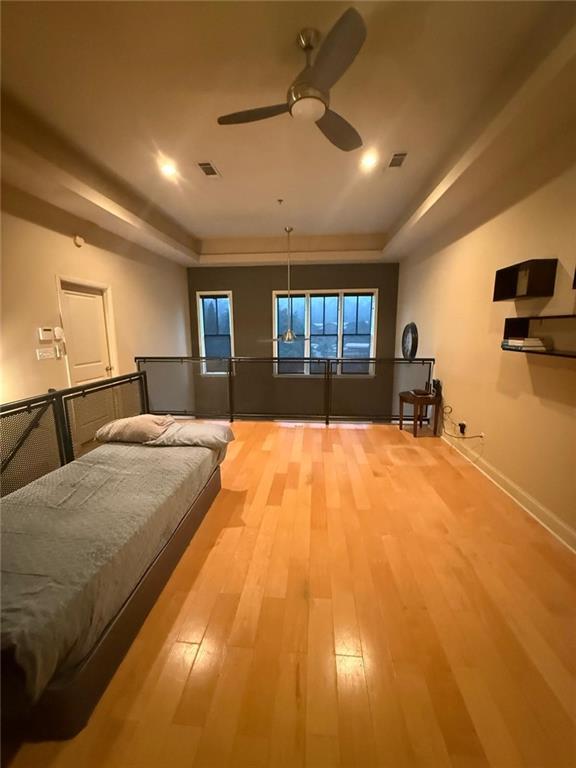 bedroom with ceiling fan, a raised ceiling, and light hardwood / wood-style flooring