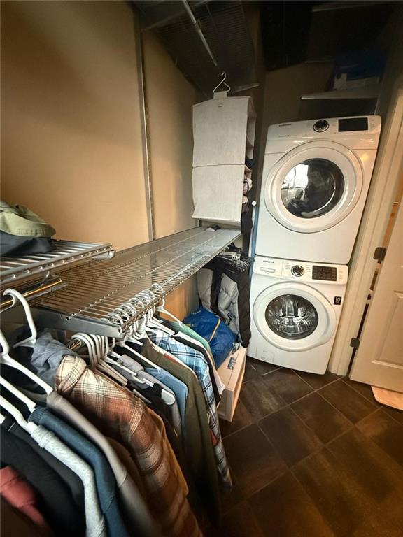 laundry area with dark tile patterned flooring and stacked washer and clothes dryer