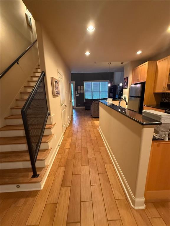 kitchen with stainless steel refrigerator, decorative light fixtures, light brown cabinetry, and sink