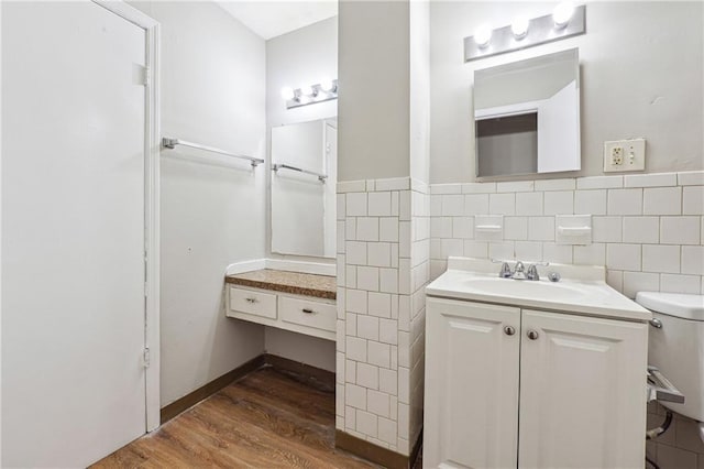 bathroom with toilet, tile walls, vanity, wood finished floors, and a wainscoted wall