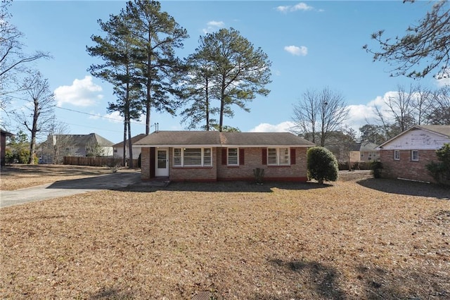 view of front facade featuring brick siding, driveway, fence, and a front lawn