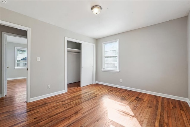 unfurnished bedroom featuring multiple windows, baseboards, and wood finished floors