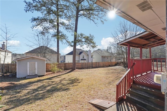 view of yard with visible vents, a deck, a fenced backyard, a storage unit, and an outbuilding
