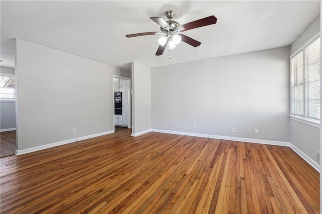 unfurnished room featuring baseboards, hardwood / wood-style flooring, a ceiling fan, and a textured ceiling