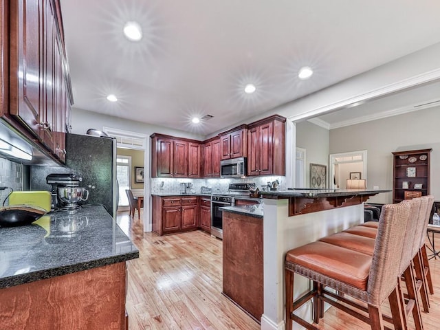 1076 Pinyan Ln, Canton, GA 30115 - kitchen featuring appliances with stainless steel finishes, a peninsula, a breakfast bar area, tasteful backsplash, and light wood-style flooring