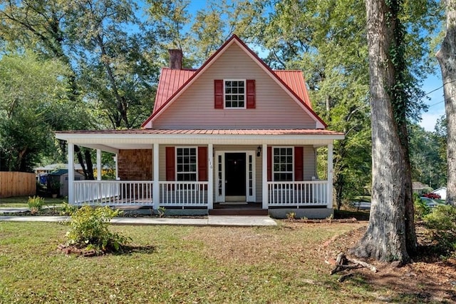 view of front facade with metal roof, a chimney, covered porch, and a front lawn