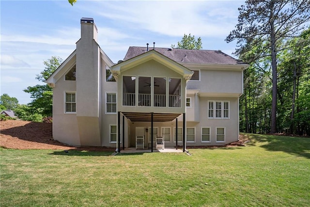 rear view of house with ceiling fan, a chimney, a yard, a patio, and stucco siding