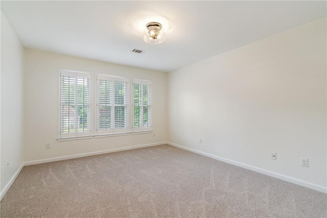 spare room featuring baseboards, light colored carpet, and visible vents
