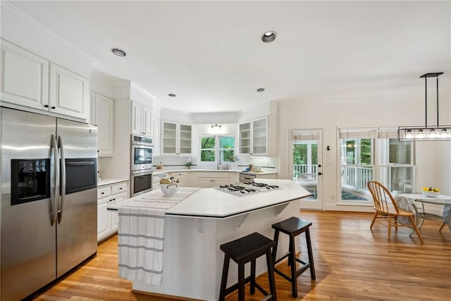 kitchen with white cabinets, light countertops, a breakfast bar area, stainless steel appliances, and glass insert cabinets