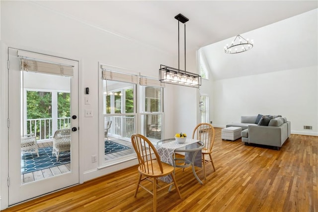 dining space with a notable chandelier, visible vents, baseboards, wood finished floors, and vaulted ceiling