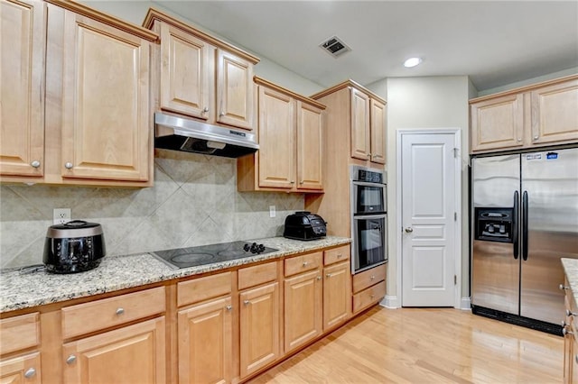 kitchen featuring light stone counters, light hardwood / wood-style flooring, light brown cabinets, stainless steel appliances, and decorative backsplash