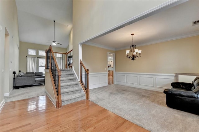 carpeted foyer featuring crown molding, ceiling fan with notable chandelier, and a high ceiling