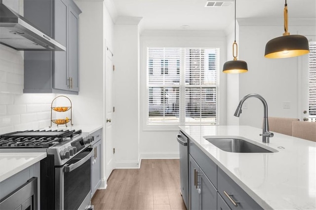 kitchen with wall chimney range hood, sink, gray cabinets, hanging light fixtures, and stainless steel appliances