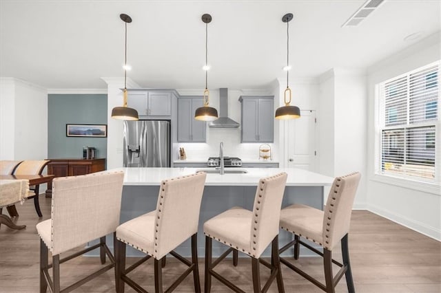 kitchen featuring gray cabinets, a breakfast bar area, stainless steel fridge with ice dispenser, decorative light fixtures, and wall chimney exhaust hood