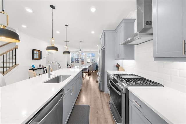 kitchen with sink, hanging light fixtures, gray cabinets, stainless steel appliances, and wall chimney range hood