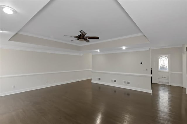 unfurnished room featuring visible vents, dark wood-type flooring, a tray ceiling, crown molding, and baseboards