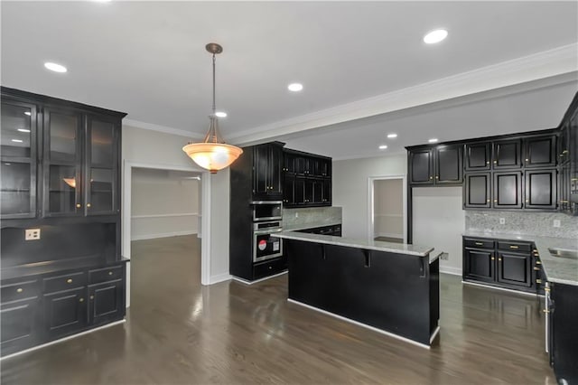 kitchen featuring dark cabinetry, light stone countertops, ornamental molding, backsplash, and a center island