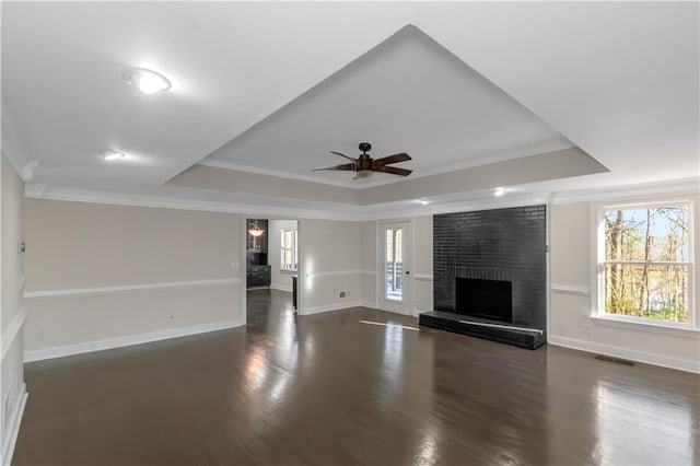 unfurnished living room featuring a tray ceiling, a brick fireplace, visible vents, and a healthy amount of sunlight