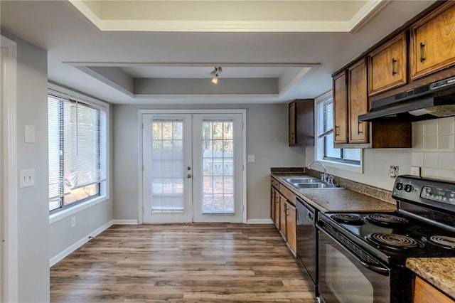 kitchen featuring french doors, light wood-type flooring, a raised ceiling, sink, and black appliances