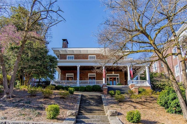 view of front of house with a porch, stairway, brick siding, and a chimney