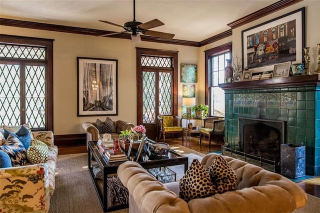 living room featuring a ceiling fan, wood finished floors, baseboards, a tile fireplace, and ornamental molding