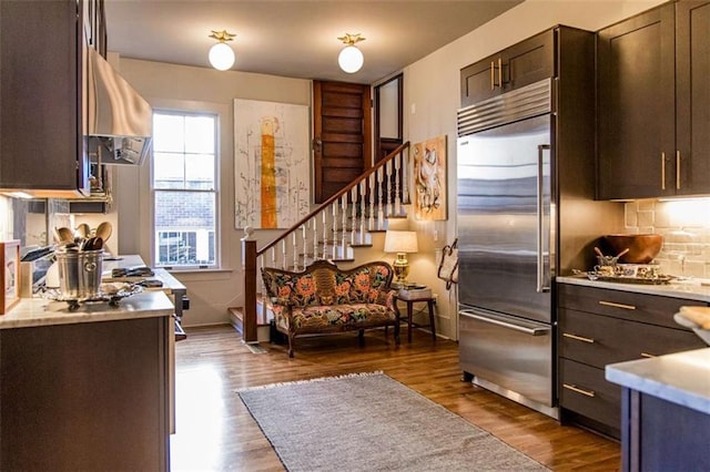 kitchen with stainless steel built in refrigerator, dark wood finished floors, ventilation hood, dark brown cabinetry, and light countertops