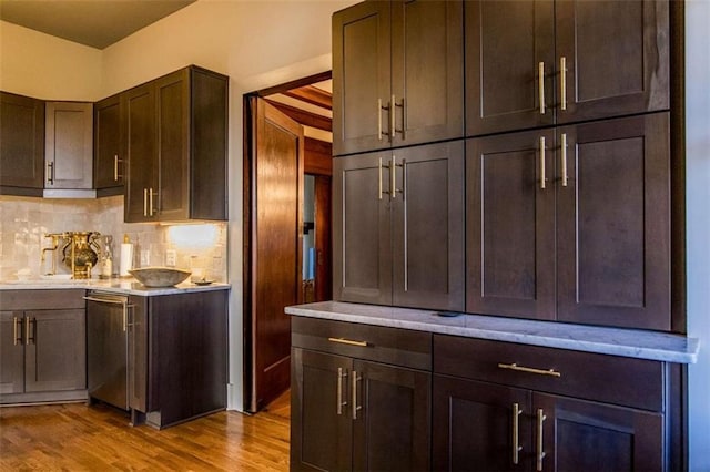 kitchen featuring dark brown cabinetry, decorative backsplash, light countertops, and wood finished floors