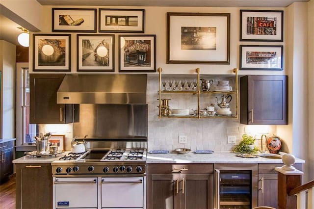 kitchen with glass insert cabinets, wall chimney range hood, beverage cooler, range with two ovens, and decorative backsplash