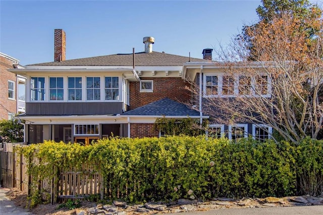 back of house featuring brick siding, a chimney, roof with shingles, and fence