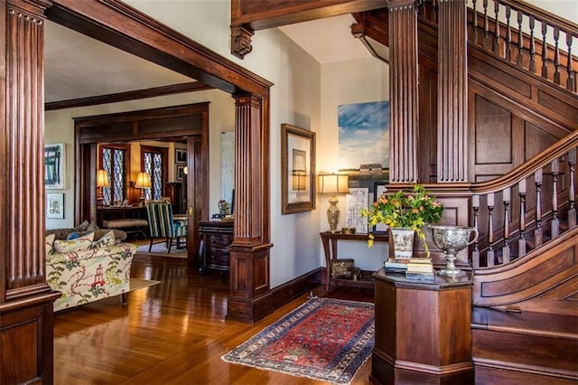 foyer entrance featuring crown molding, baseboards, stairway, decorative columns, and wood finished floors