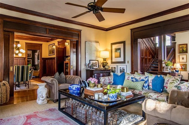 living area with crown molding, stairs, wainscoting, wood finished floors, and a ceiling fan