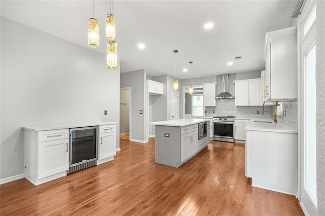 kitchen featuring white cabinetry, a center island, wall chimney range hood, and appliances with stainless steel finishes