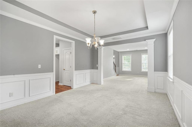 carpeted spare room with a chandelier, a raised ceiling, crown molding, and decorative columns