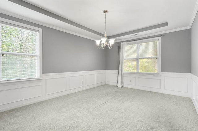 carpeted empty room with plenty of natural light, a raised ceiling, ornamental molding, and a chandelier