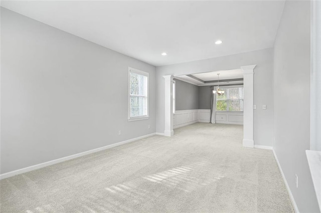 carpeted spare room featuring decorative columns and a chandelier