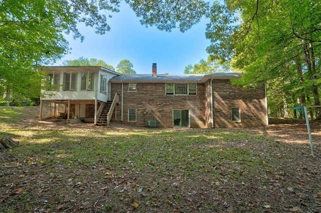 back of property with stairs, a chimney, a sunroom, and a yard