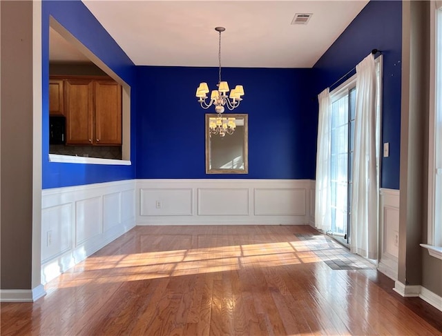 unfurnished dining area featuring a notable chandelier, a healthy amount of sunlight, and light hardwood / wood-style flooring