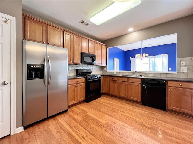 kitchen with black appliances, light wood-type flooring, backsplash, decorative light fixtures, and a notable chandelier