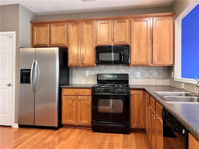 kitchen with decorative backsplash, black appliances, sink, and light wood-type flooring