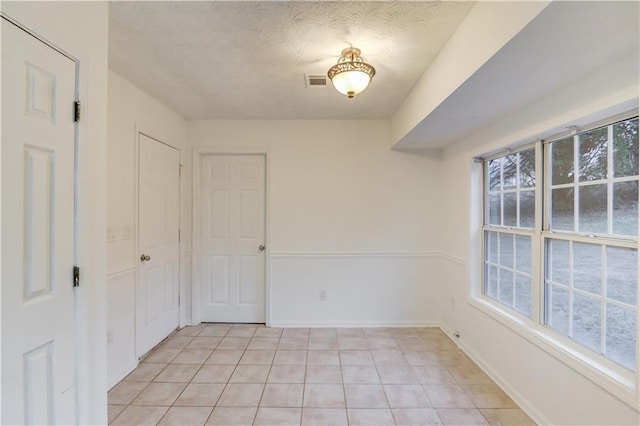 spare room with a textured ceiling, plenty of natural light, visible vents, and baseboards