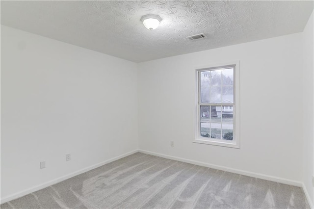 spare room featuring light colored carpet, visible vents, baseboards, and a textured ceiling