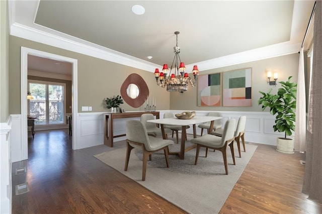 dining area featuring a decorative wall, wood finished floors, wainscoting, and crown molding