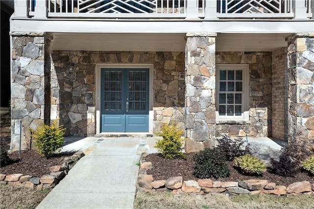 view of exterior entry with stone siding, a balcony, and a porch