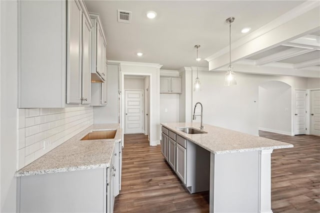 kitchen with a kitchen island with sink, hanging light fixtures, sink, light stone counters, and dark hardwood / wood-style flooring