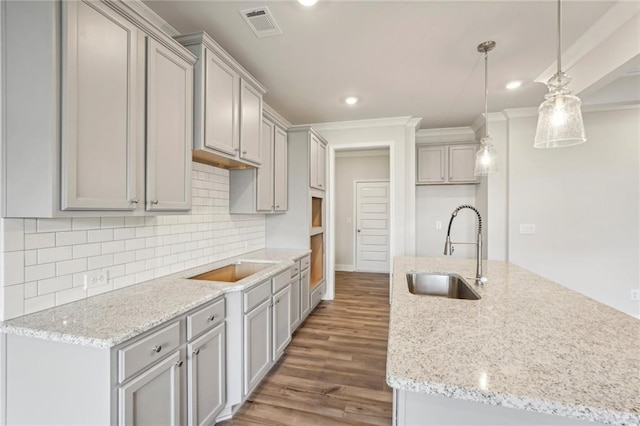 kitchen featuring dark hardwood / wood-style floors, crown molding, sink, light stone countertops, and pendant lighting