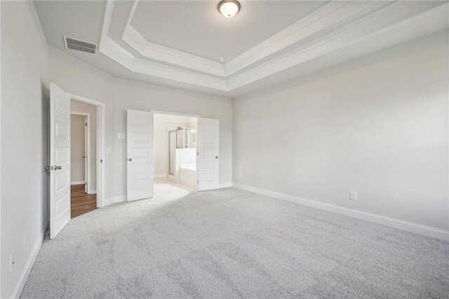 unfurnished bedroom featuring ensuite bath, a tray ceiling, and carpet